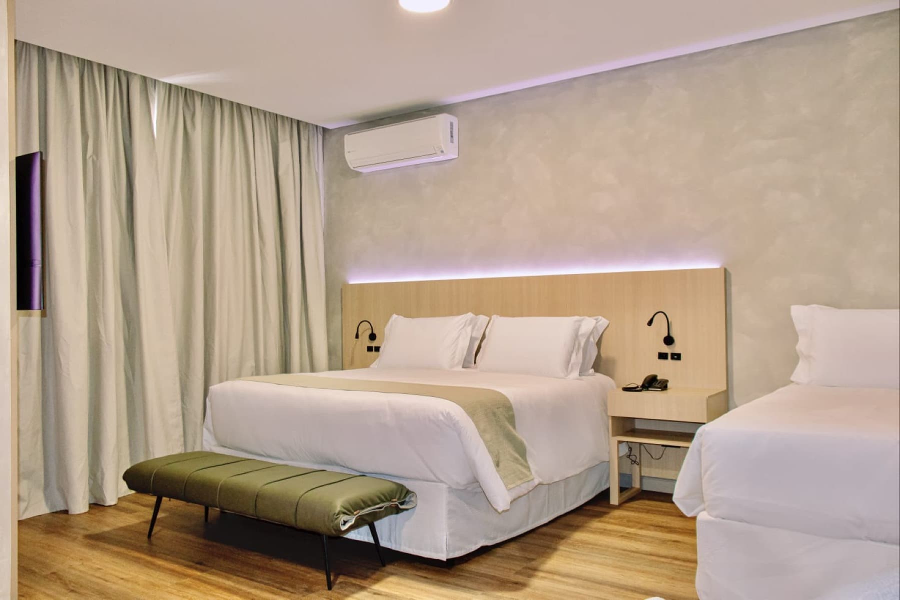 Suíte com cama king, luz indireta dourada e poltrona verde-oliva